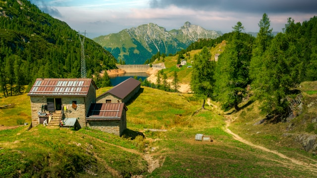 Rustic wooden cabin with solar panels on a grassy hillside overlooking a lake and mountains — ideal example of best land for off-grid living with water access, solar potential, and legal road access.