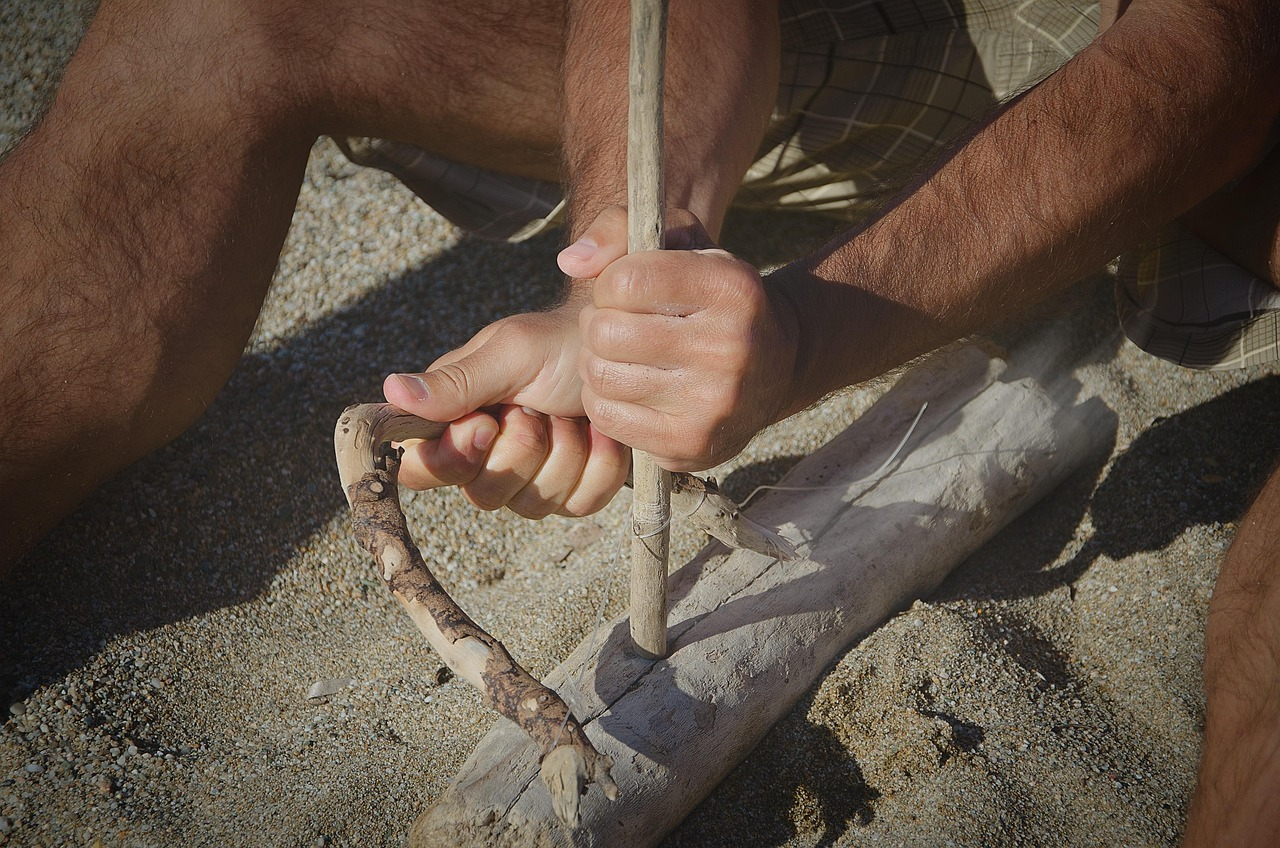 Bow drill fire starting: hands using primitive wooden bow and spindle to create friction fire in wet weather